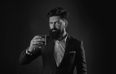 Siyah takım elbiseli, çatı katında viski bardağı olan kendine güvenen sakallı adam. Camdan alkol içen adam