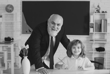 Yaşlı öğretmen ve genç öğrenci veya okul çocuğu. Öğrenci sınıfta öğretmenle okuma yazma öğreniyor.