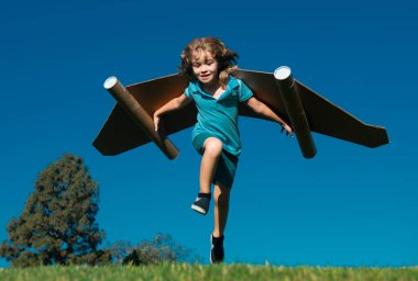 Mavi gökyüzüne doğru uçan kağıt kanatlı mutlu çocuk. Oyuncak jetpack ile oynayan bir çocuğun portresi. Özgürlük tasasız, başarı kazanan, yenilik ve hayal gücü kavramı