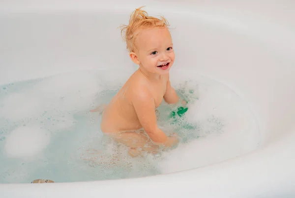 Funny cheerful toddler cleaning body in the bath. Little boy in bathtub with fluffy soap bubble