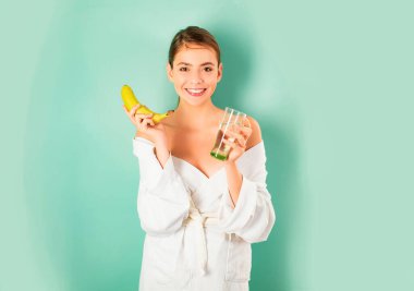 Güne gülümseyerek başla. Su dengesi. Kadın bornozu, bir bardak su ve muz. Sabah alışkanlığı su içer. Sağlık hizmeti konsepti. Sağlık ve güzellik. Spa ve sağlık. Kız su dengesini önemser..