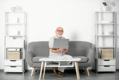 Üst düzey ofis çalışanının dizüstü bilgisayarlı portresi. Gri sakallı yaşlı adamın evde ya da ofiste bir dizüstü bilgisayarda işi var. Bilgisayar kullanan olgun yaşlı bir adam. Yaşlı genel müdür.