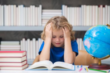 Yorgun okul çocuğu, okulda sıkılmış öğrenci. Okulda kitap okuyan bir öğrenci. Ödev yapan bir çocuk, kitapların olduğu masada oturuyor, sınıfta.