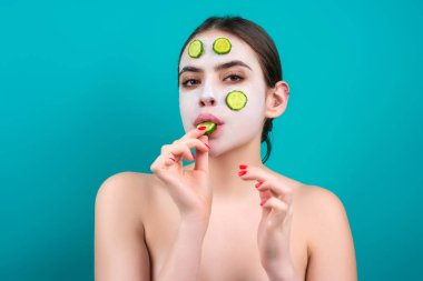 Close up beauty portrait of a beautiful woman applying face cream and facial mask of cucumber. Mask for skin lifting and anti-aging effect, studio background. Anti aging cream. Facial treatment