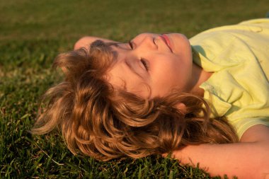 Çim tarlasında gülümseyen mutlu bir çocuğun portresi. Çocuklar rüya görüyor. Yaz rüyası. Çocuk çimenlerde rüya görüyor. Çocukluk rüyası. Hayalperest çocuk. Hayaller ve hayal gücü. Rüya gibi çocuklar.