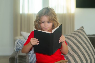 Eğitim kavramı, çocukluk, kitap okuma, sanat eseri, ilham. Odadaki kanepede uzanmış kitap okuyan sıradan giyinmiş tatlı bir çocuk.