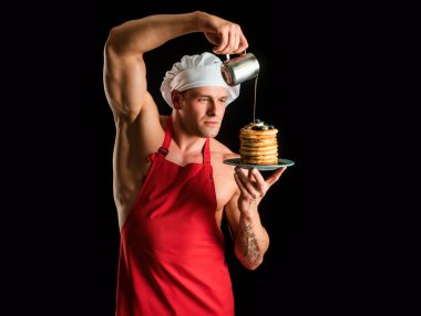 Sexy cook or baker in chefs hat with sweet homemade stack of pancakes with syrup. Chef muscle man with apron bake pancakes with berries and maple syrup