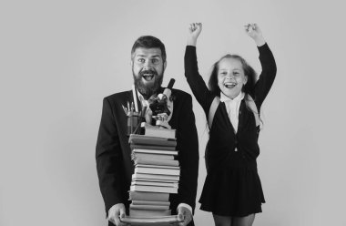 Baba ya da öğretmenin elinde okul kitaplarının büyük yığını var. Okula geri dön, üniformalı öğrenci kız. Elinde kitap yığını olan küçük bir kız. Çalışması zor.