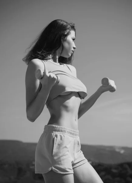 空を背景にダンベルと働く強い女性 トレーニング中のフィットネス女性 強い腹筋 — ストック写真