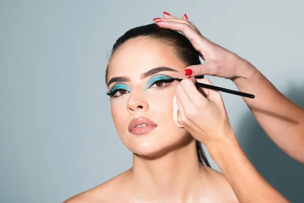Beautiful woman face with perfect makeup. Makeup artist applies eye shadow. Hand of visagiste, painting cosmetics of young beauty model girl. Beauty girl with perfect skin