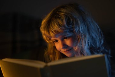 Evde yatakta kitap okuyan bir çocuk. Yatmadan önce masal masalı. Okul rüyası. Hayalperest okul çocuğu. Hayaller ve hayal gücü. Hayalci okul çocuğu suratı.