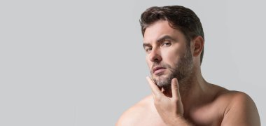 Bin yıllık İspanyol adam banyoda aynaya, yüz derisine ve sakalına bakıyor. Erkek güzellik ürünleri. Cilt bakımı, spa. Güzel bir adamın güzel portresi. Spa, nemlendirici besleyici krem
