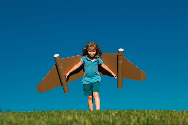 おもちゃのジェットパック屋外の子供 子供は青い空に紙の翼で走る 未来の子供の夢 子供のパイロットの夢 夢のコンセプト ブロンドのかわいい空想家の子供が飛ぶことを夢見ている 夢と想像力 — ストック写真