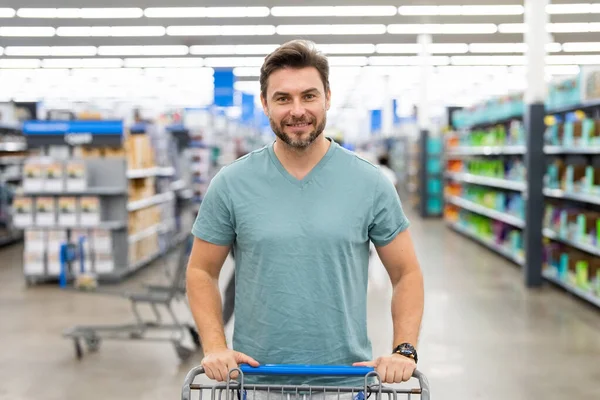Handsome man with shopping basket with shopping trolley at grocery. Man buying groceries in supermarket. Male model in shop. Concept of shopping at supermarket