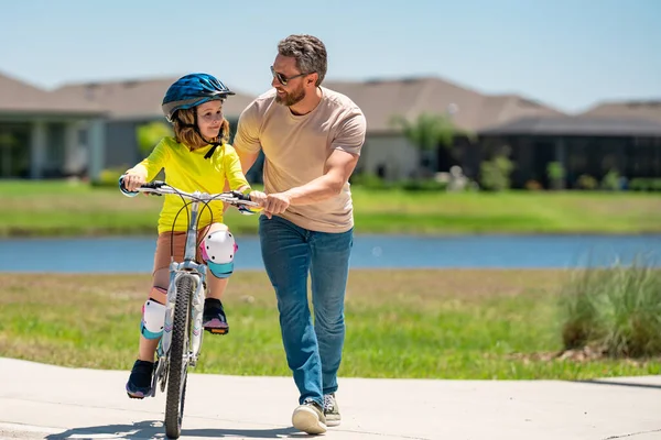 父亲节 男孩和他的父亲在公园里学习骑自行车 爸爸教他儿子骑自行车 父亲学着小儿子骑自行车 父亲抚养孩子 父亲节背景 — 图库照片