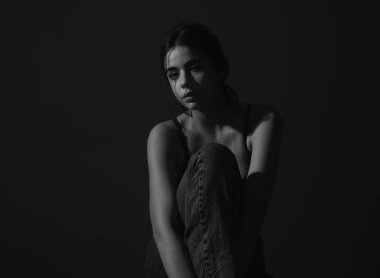 Kot pantolonlu, siyah sütyenli, seksi bir kadın oturuyor ve kameraya bakıyor. İzole edilmiş gri