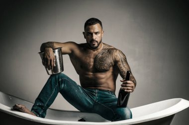 Şampanya kutlaması. Gri arka planda dövmeli yakışıklı bir adam. Seksi gece partisi, genç aşıklar. Kot pantolonlu moda adamı bacakları