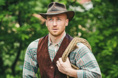 Yeşil arka planda kement ipi olan bir kovboy. Batı hayatı. Yakışıklı sakallı batı çiftçisi. Kovboy ya da çiftçi portresi. Batı