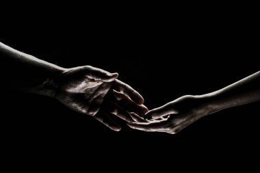 Two hands reaching toward. Helping hand outstretched for salvation on isolated black background. Close up of man and woman hand touch with fingers. Man and woman holding hands