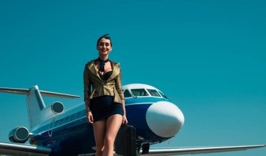 Hostes ve seyahat zamanı. Uçak arka planında servis yapan gülümseyen hostes portresi. Uçuş görevlisi üniforması. Uçak yolculuğu. Hostes kadın. Boşluğu kopyala, mavi üzerine izole edilmiş