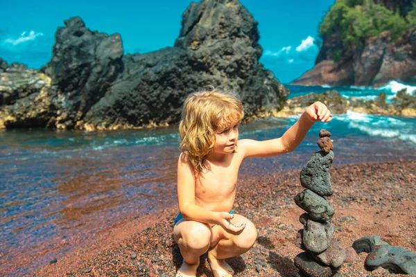 海のそばに火山岩の上に小石を作るかわいい少年が積まれています 禅の概念 — ストック写真