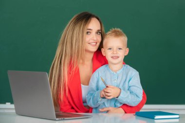 Öğretmen okulda okul çocuğuna yardım ediyor. Anne ve oğlu birlikte bilgisayar laptopu kullanıyorlar. Okul çocuğu çevrimiçi eğitim öğreniyor