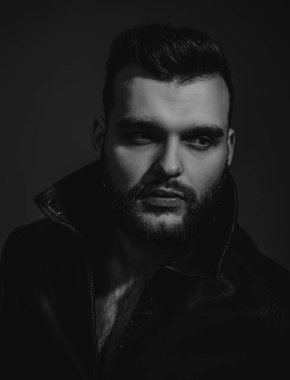 Yakışıklı bir gencin portresi. Eski moda kıyafetler, eski moda deri ceket. Erkeklik kavramı. Saç stili olan vahşi sakallı motorcu. Çekici erkek.