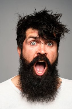 Sakallı ve bıyıklı bir adam. Şaşırmış ve heyecanlı görünüyor. Erkek saç kesimi, modern saç stili. Uzun saçlı erkek modelin yakın portresi. Sağlık ve saç bakımı sabah konsepti