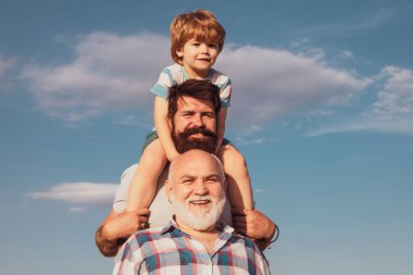 Babalar Günü. Büyükbaba, baba ve oğul kucaklaşıp birlikte eğleniyorlar. Mutlu çocuk yaz gökyüzü arka planında oynuyor