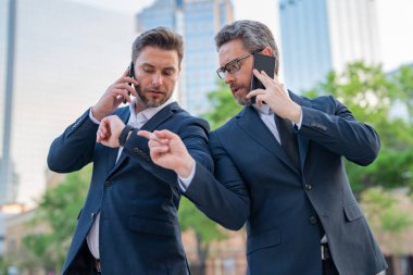 Şehirdeki arka planda çalışan beyaz bir çalışan cep telefonundan mesaj yolluyor. Açık havada akıllı telefon kullanan resmi takım elbiseli bir iş adamı.