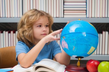 School kid pupil looking at globe in library at the elementary school. World globe. School child 7-8 years old with book go back to school. Little student