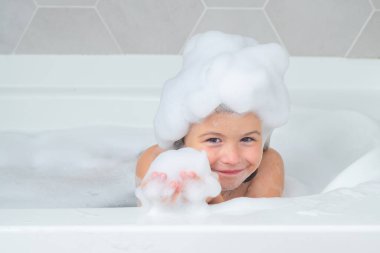 Çocuk kafasında sabun. Köpüklü çocuk yüzü. Şampuan köpüğü ve banyo yapan saçlarında kabarcıklar olan bir çocuk. Gülümseyen çocuk portresi, saç bakımı ve hijyen. Çocuklar uzun saçlar için şampuan kullanırlar. Banyoda saç yıkamak.