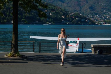 Woman tourist walking on street, summer fashion style, travel to Europe. Fashion tourist. Elegant woman tourist in trendy dress near jet. Travel tourist in Como lake Italy