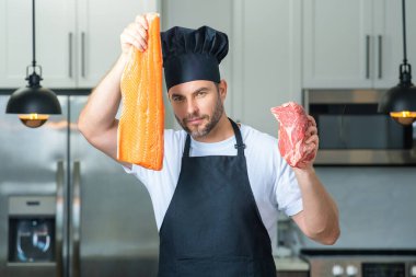 Aşçı portresi. Mutfakta balık, et, somon ve sığır eti var. Önlük, şef üniforması ve aşçı şapkası takan bir adam. Çiğ et ve balık fileto. Yüksek protein diyeti