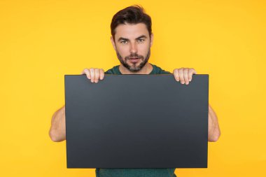 Stüdyonun arka planında boş tahtası olan yakışıklı bir adam. Telif uzayı ile boş tabela gösteren bir adam. Fikir teklifi. Reklamınız. Metin için boş alanı olan boş reklam panosu, modelle