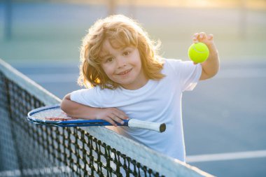 Tenis raketi ve tenis topu olan çocuk tenis kortunda oynuyor.