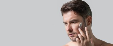 Bin yıllık İspanyol adam banyoda aynaya, yüz derisine ve sakalına bakıyor. Erkek güzellik ürünleri. Cilt bakımı, spa. Güzel bir adamın güzel portresi. Spa, nemlendirici besleyici krem