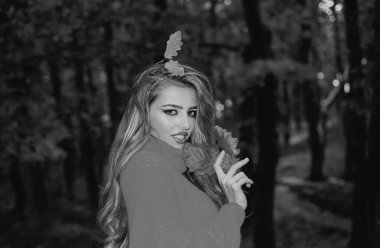 Güneşli bir sonbahar gününde parkta mutlu bir genç kadın. Sonbahar gününde poz veren tatlı bir kız. Güz yapraklarıyla çevrili güzel bir bayanın açık hava moda fotoğrafı. Sonbahar manzarası