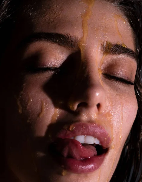 Sensual young woman face with honey drop close up. Sexy model with honey drip on face