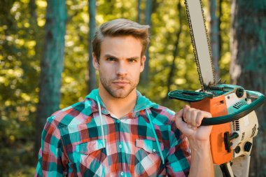 Erkek işi yapan adam. Oduncu ciddi bir yüz üzerinde testere taşır. Ormanların yok olması, doğal ekosistemlerin toprak bozulması ve istikrarsızlaşmasının önemli bir nedenidir.