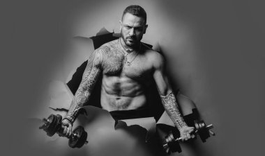 Çıplak gövdeli genç kaslı adam spor salonunda çalışıyor. Stüdyoda pazı kaldıran bir sporcu. Egzersiz yapan atletik adam. Bayrak sporu. İnsan gücü