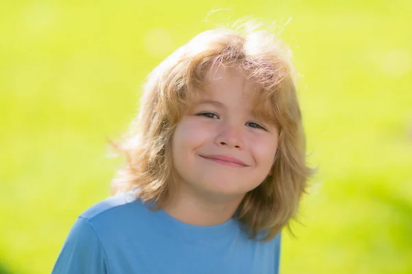 Funny kids emotions. Outdoor close up portrait of a cute little child playing outdoor. Cute funny blonde little child close up portrait on green grass background