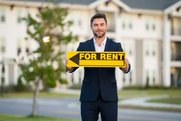 Real estate agent hold house rent sign. Real estate renting property. Rent new home. Handsome real estate agent in suit showing the house for rent. Rent home, rental concept. Renting an apartment