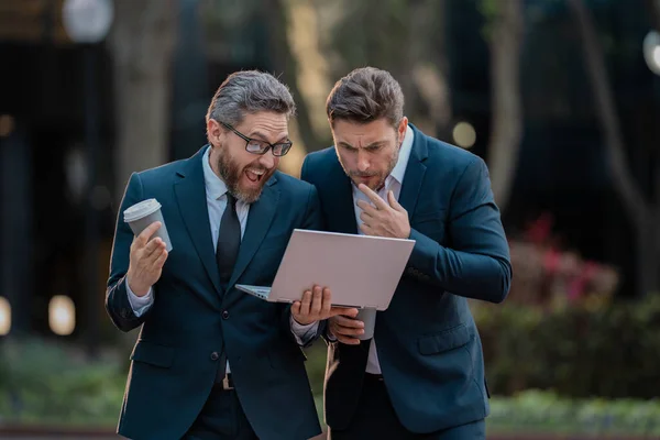 Two business man using laptop outdoor. Business men team using laptop outdoor. Businessmen looking laptop with their business success in city background. Two business teams success