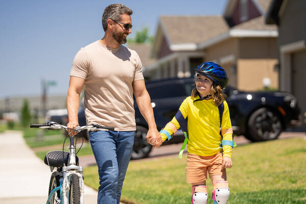 Отец учит сына кататься на велосипеде. Отец помогает взволнованному сыну кататься на велосипеде в американском районе. Ребенок в велосипедном шлеме учится ездить на велосипеде с отцом. День отца