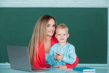 İlkokul öğretmeni ve öğrenci sınıfta. Anne ve oğlu birlikte bilgisayar laptopu kullanıyorlar.