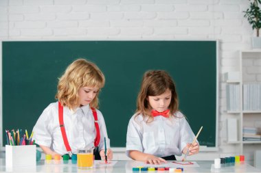 Resim okulu öğrencileri resim ödevi yapıyor. Çocuklar ilkokulda resim çiziyor. Kalem ve boyalarla çizen kardeşler.