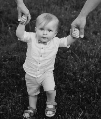 Anne ve baba el ele tutuşup yaz günü çimenlerde yürüyorlar. Yavrum, yaz tatilinin tadını çıkar.