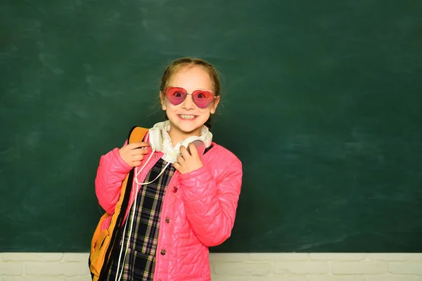 バックパック付きの笑顔の小さな小学生の女の子は 黒板に本を持っています 子供のライフスタイルの概念 学校教育 — ストック写真