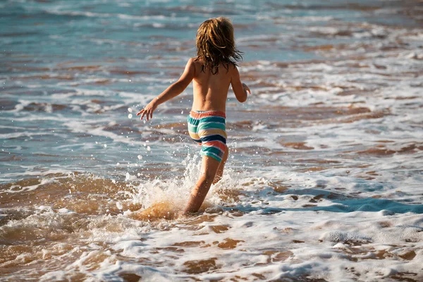 子供の男の子のバックビューは 熱帯の海のビーチで楽しんでいます 面白い子は波の端に沿ってウォータープールでスプラッシュで実行されます 夏休みのキッズアクティビティ — ストック写真
